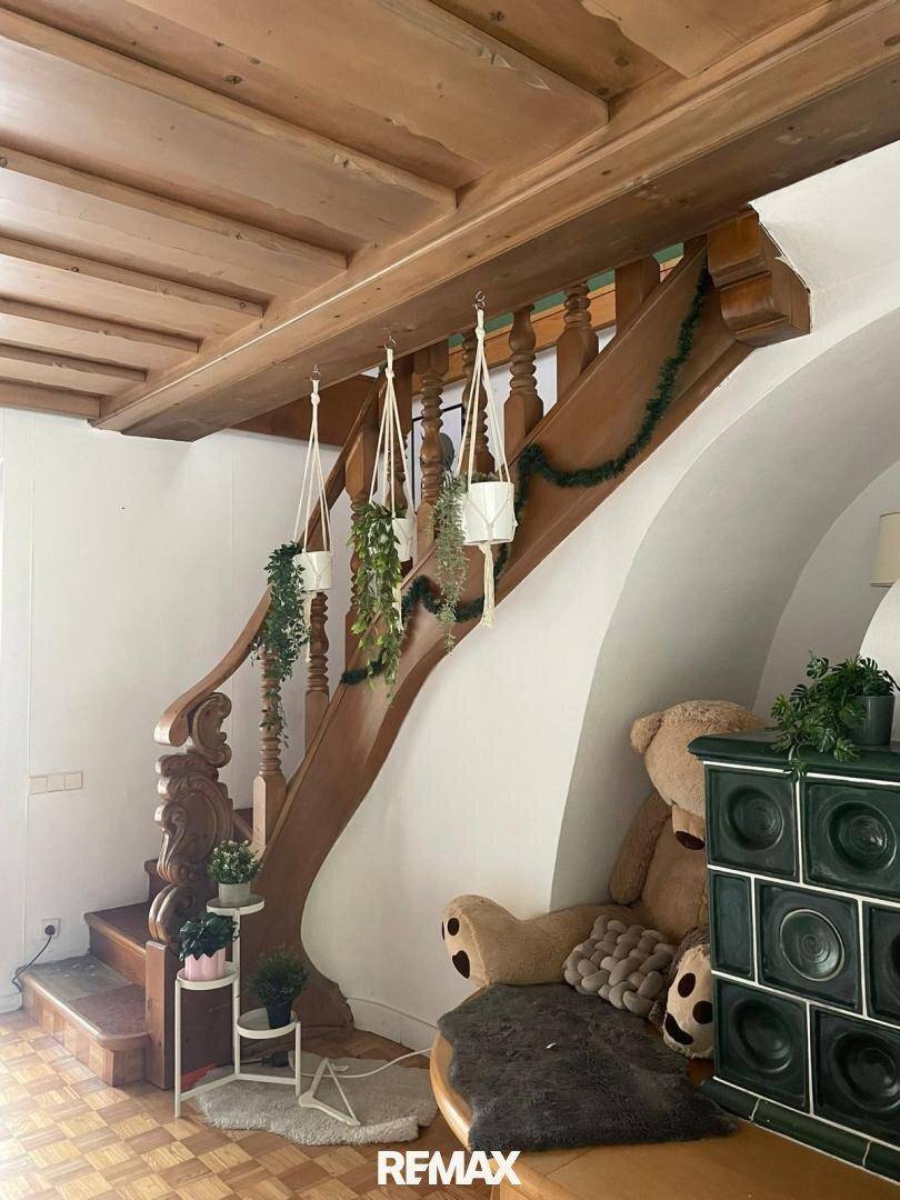 Holztreppe mit Pflanzen und traditionellem Kachelofen in einem gemütlichen Ambiente.