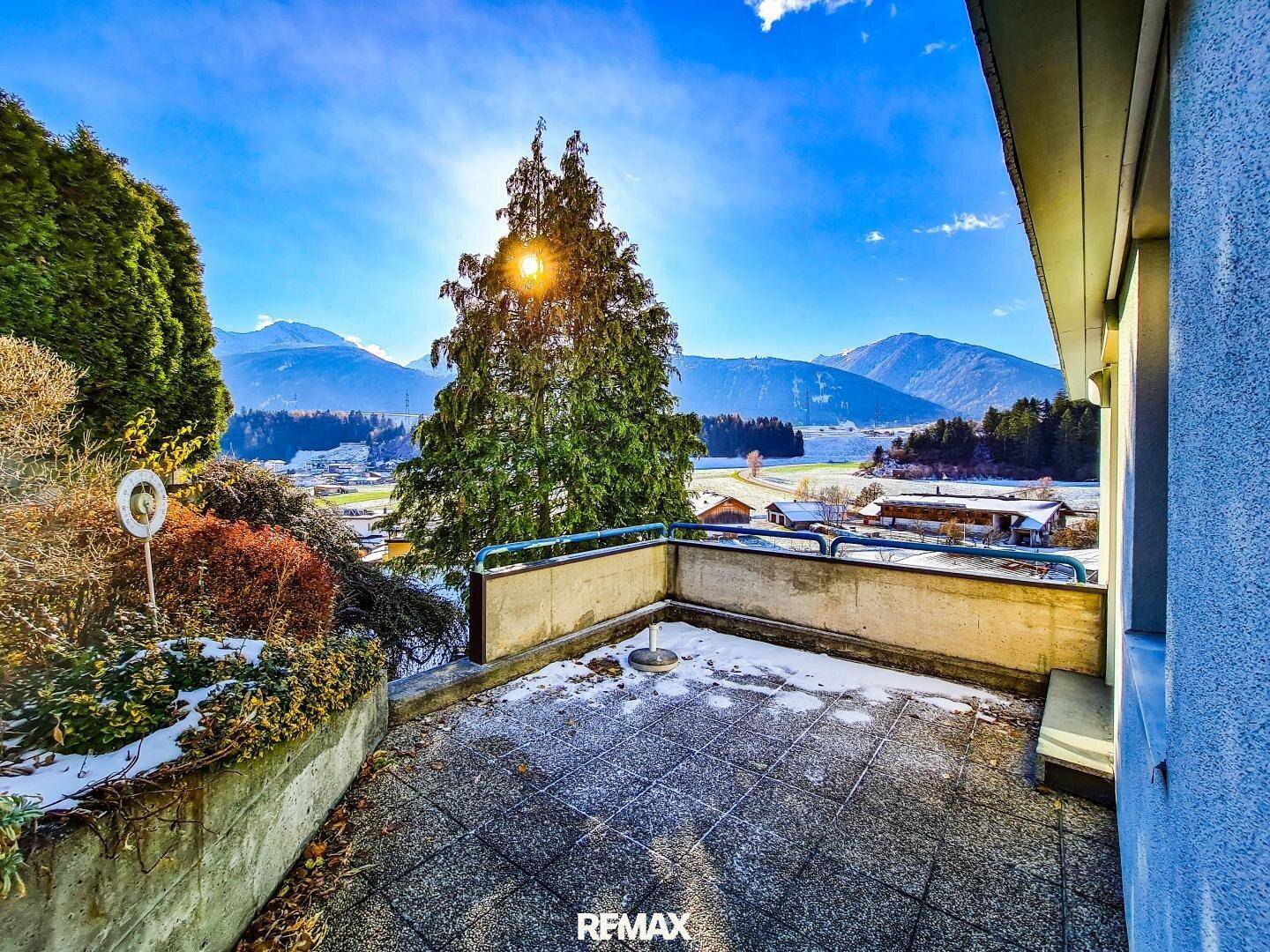 Sonniger Terrassenbereich mit Fliesenboden und weitem Panoramablick auf die umliegenden Berge.
