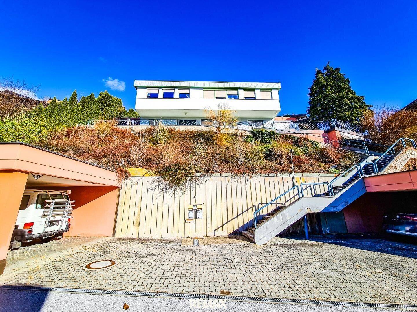 Zufahrt zum Haus mit Parkplätzen und Treppenaufgang in einer malerischen Berglandschaft.