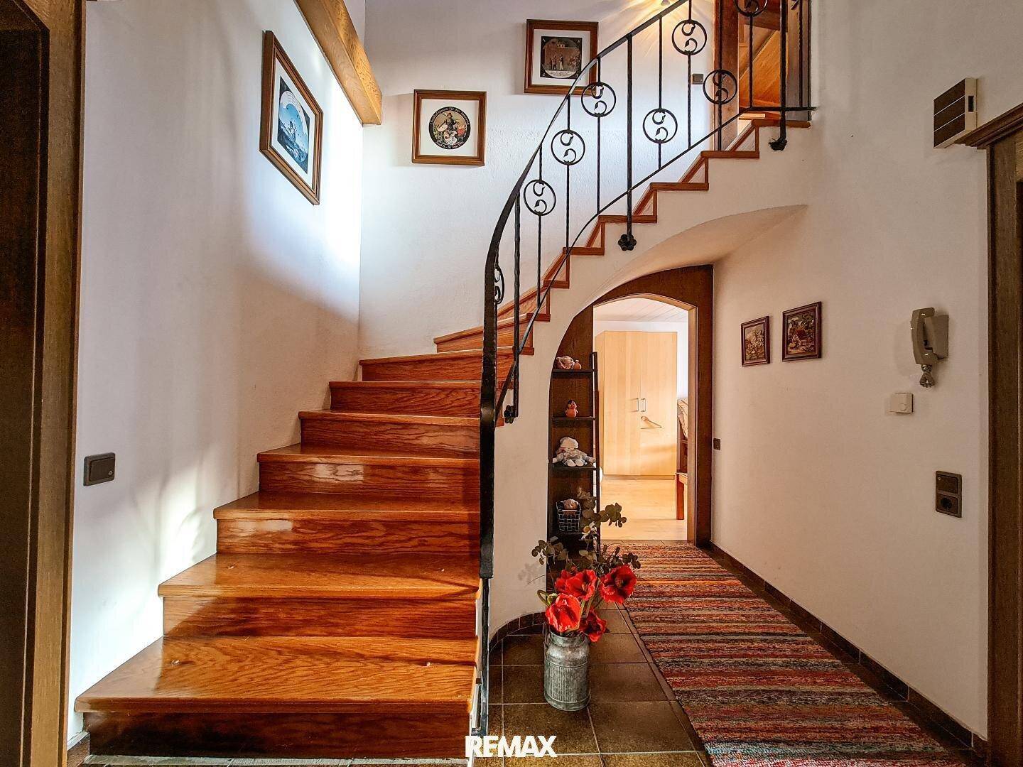 Heller Flur mit geschwungener Holztreppe und schmiedeeisernem Geländer, einladend gestaltet.