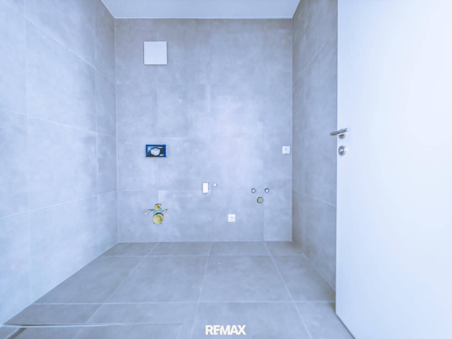 Leeres Badezimmer mit hellgrauen Fliesen an Wänden und Boden, bereit für die Installation.