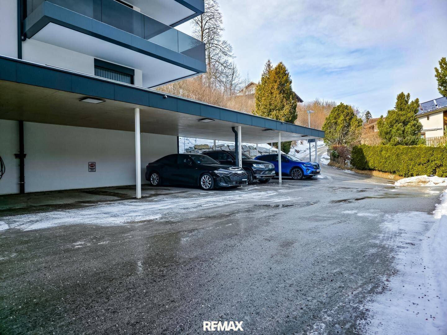Überdachte Parkplätze für mehrere Fahrzeuge vor der modernen Wohnanlage.