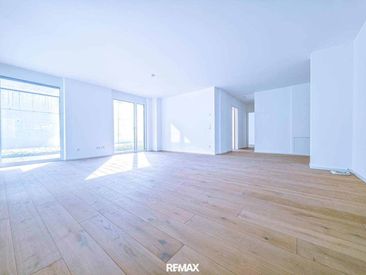 Geräumiger, heller Wohnbereich mit Holzboden und viel Tageslicht durch große Fensterfronten.