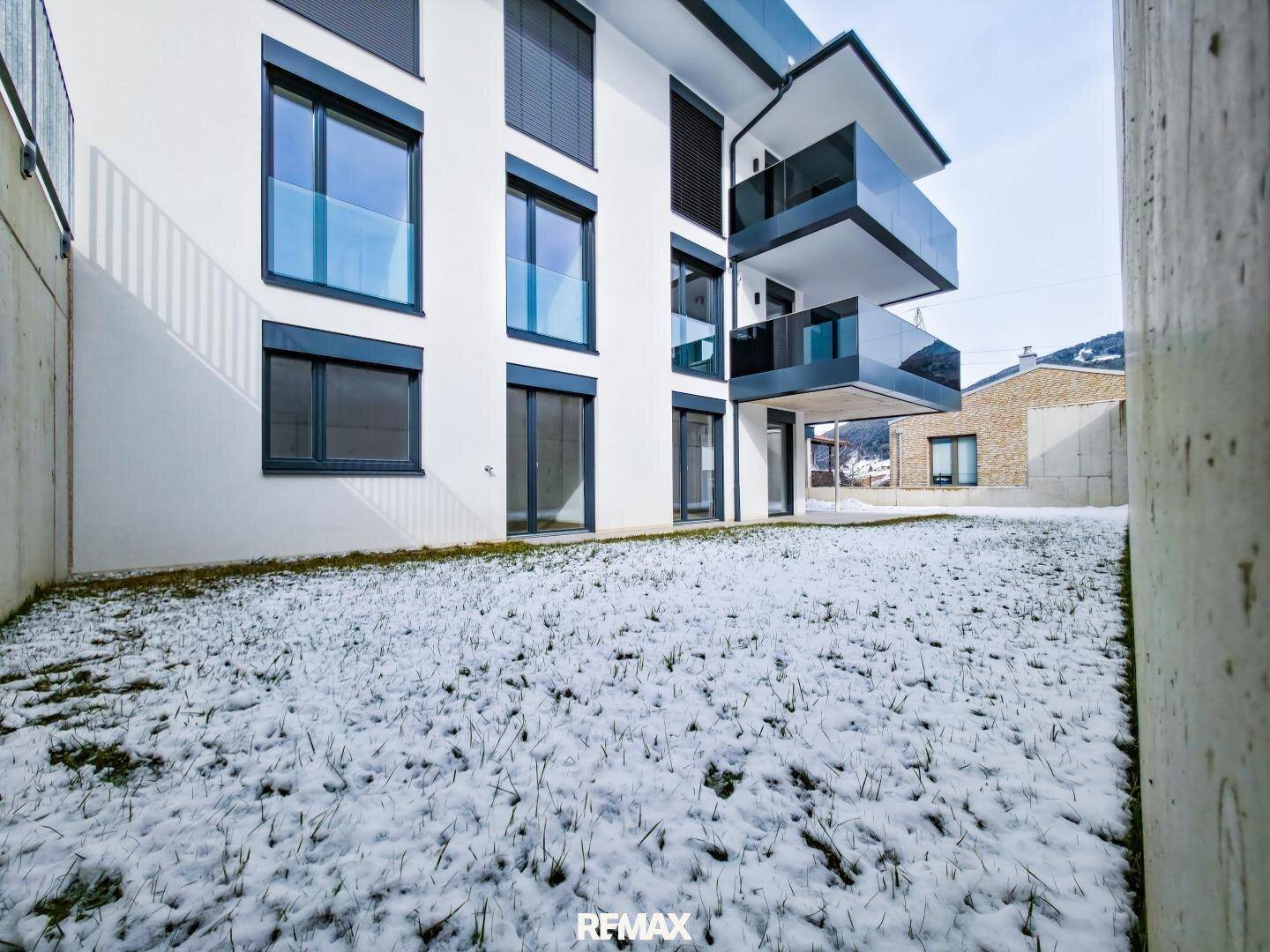 Moderne Gebäudefassade mit Balkonen und schneebedecktem Gartenbereich im Erdgeschoss.
