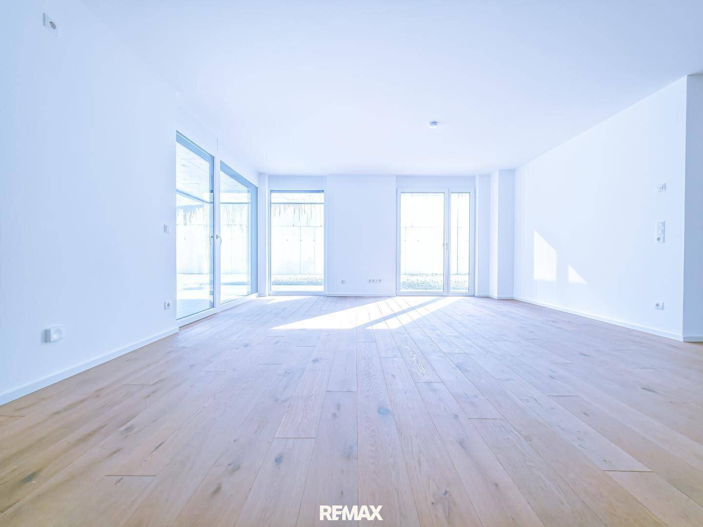 Heller, weitläufiger Wohnbereich mit Holzboden und großen Fensterfronten, die viel Licht hereinlassen.