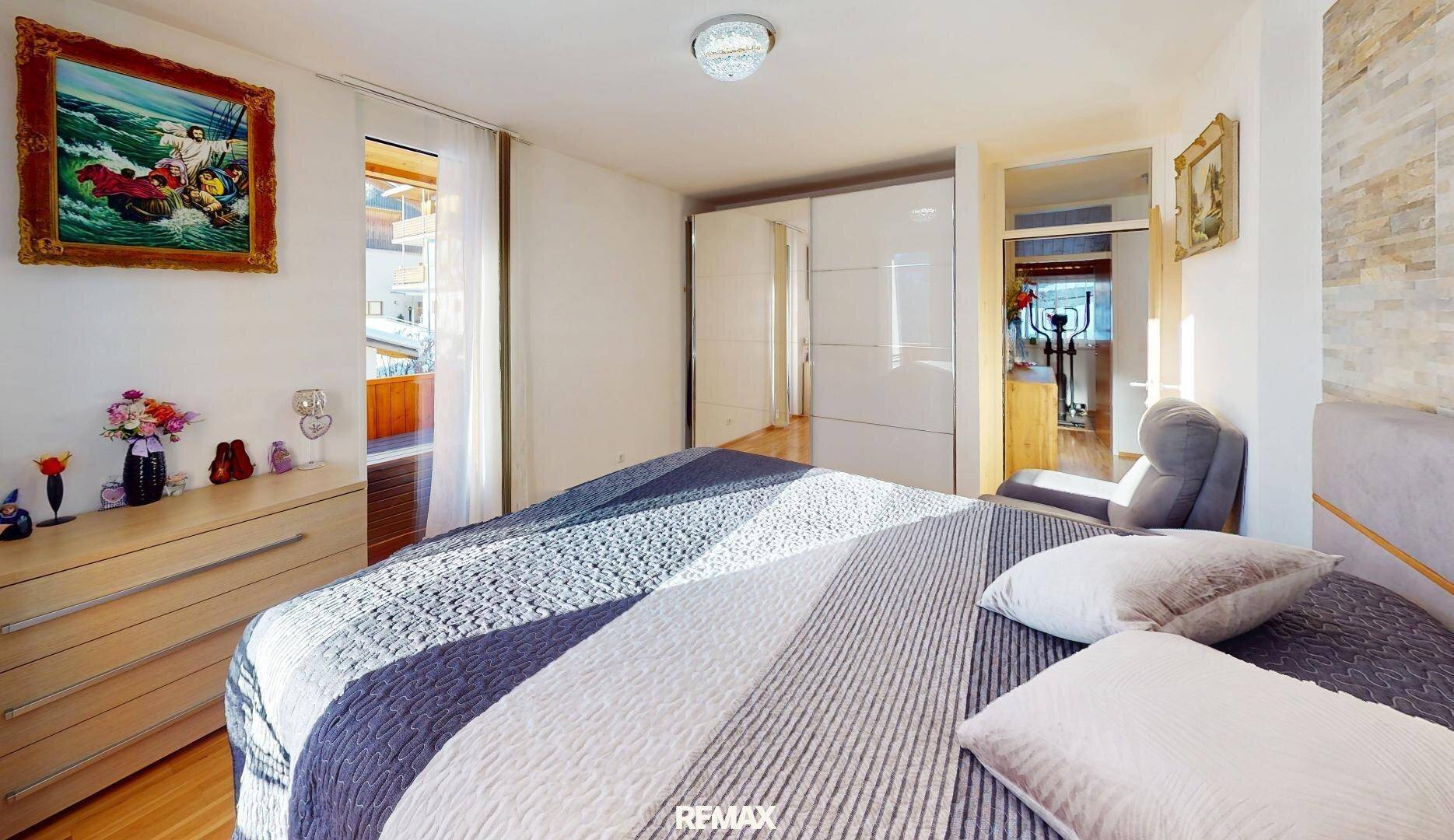 Helles Schlafzimmer mit Doppelbett, Kommode und Spiegelschränken, mit Zugang zum Balkon.