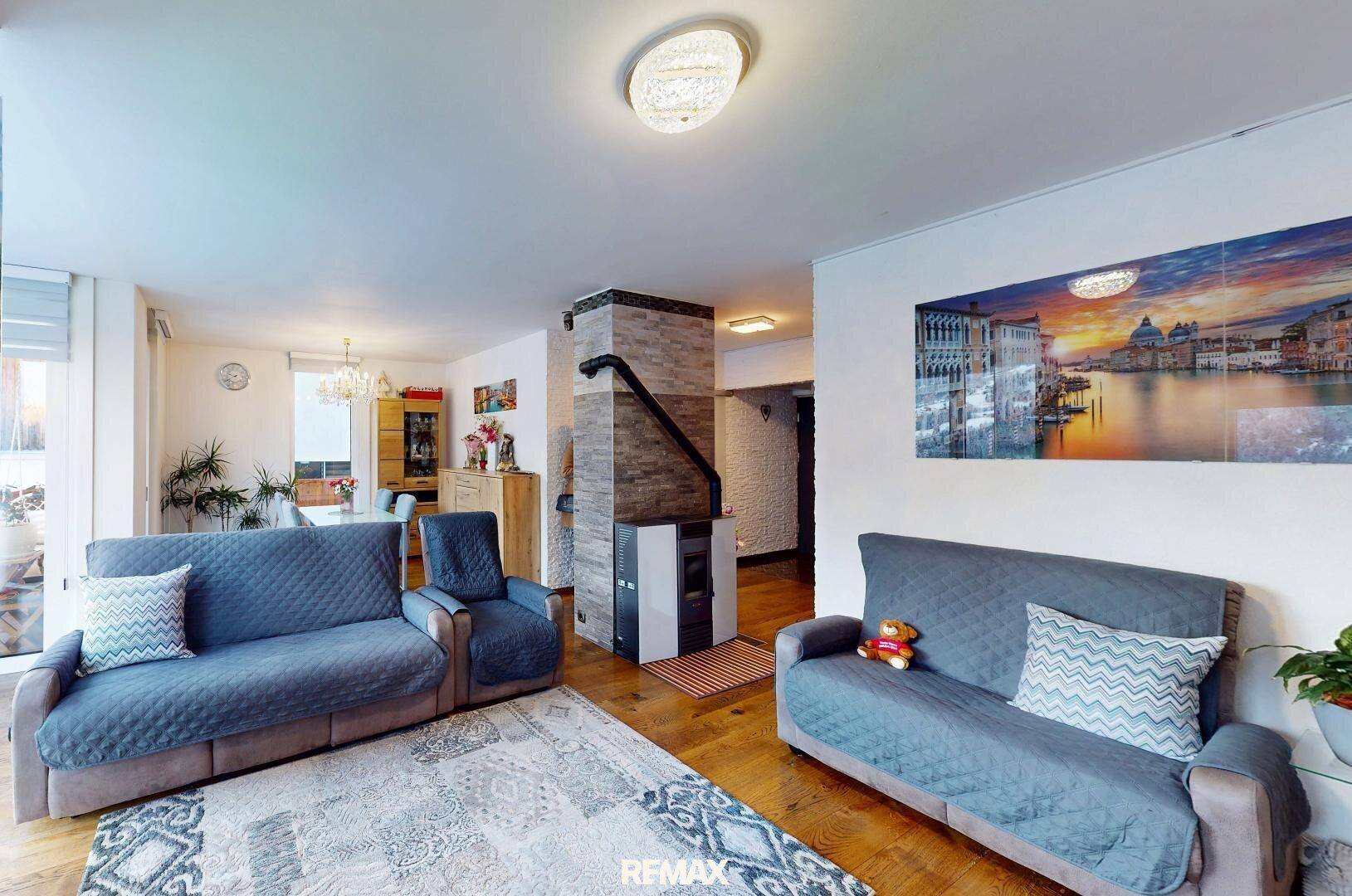 Gemütlicher Wohn-Essbereich mit Sofas, Esstisch und einem modernen Kaminofen auf Holzfußboden.