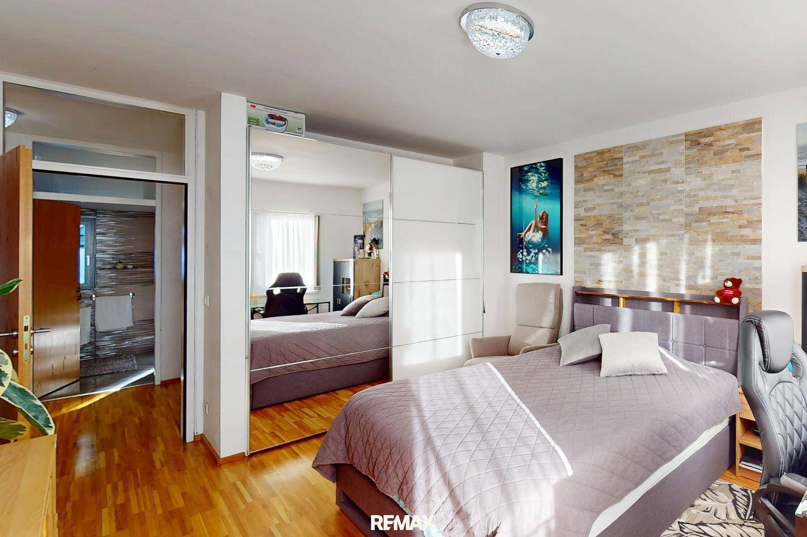 Schlafzimmer mit Bett, Spiegelschrank und Schreibtisch, mit direktem Zugang zum Badezimmer.