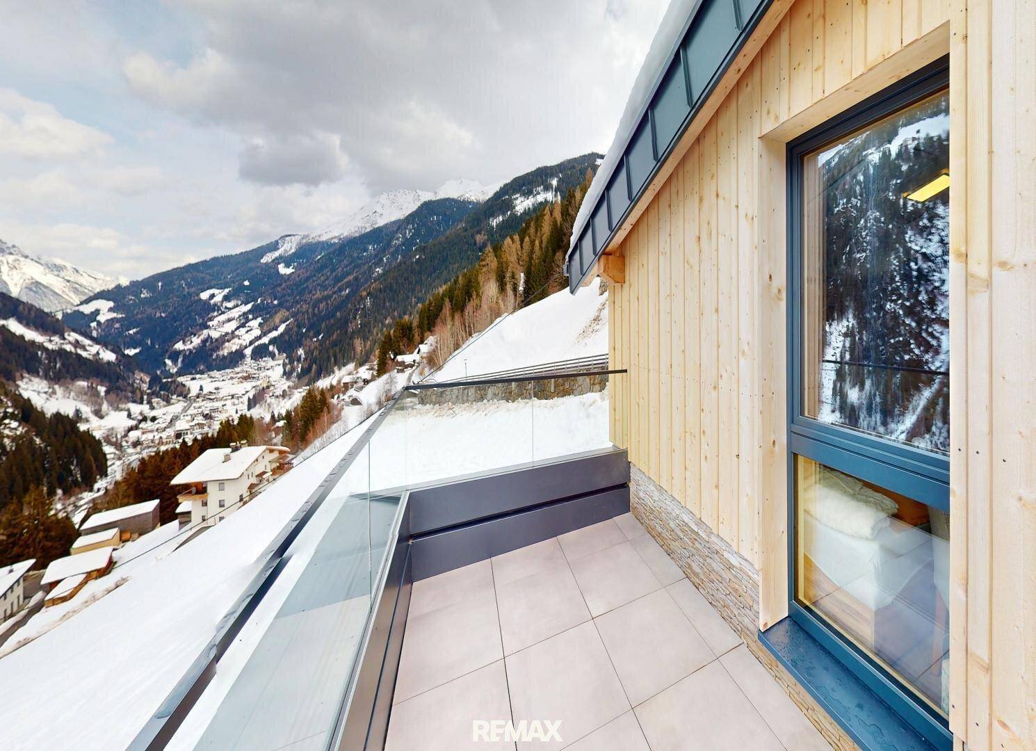 Geräumiger Balkon mit Fliesenboden und weitem Blick auf die verschneite Berglandschaft.