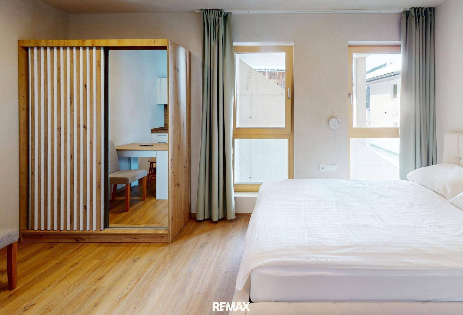 Schlafzimmer mit Doppelbett, großem Schrank mit Spiegeltür und Fenstern.