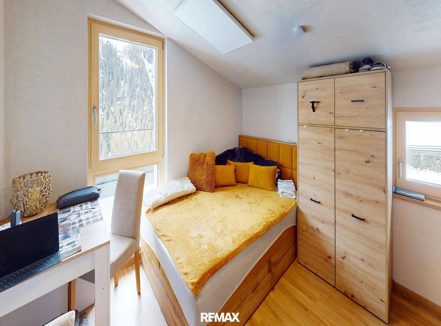 Helles Schlafzimmer mit Holzboden, großem Fenster und Blick auf die verschneite Berglandschaft.