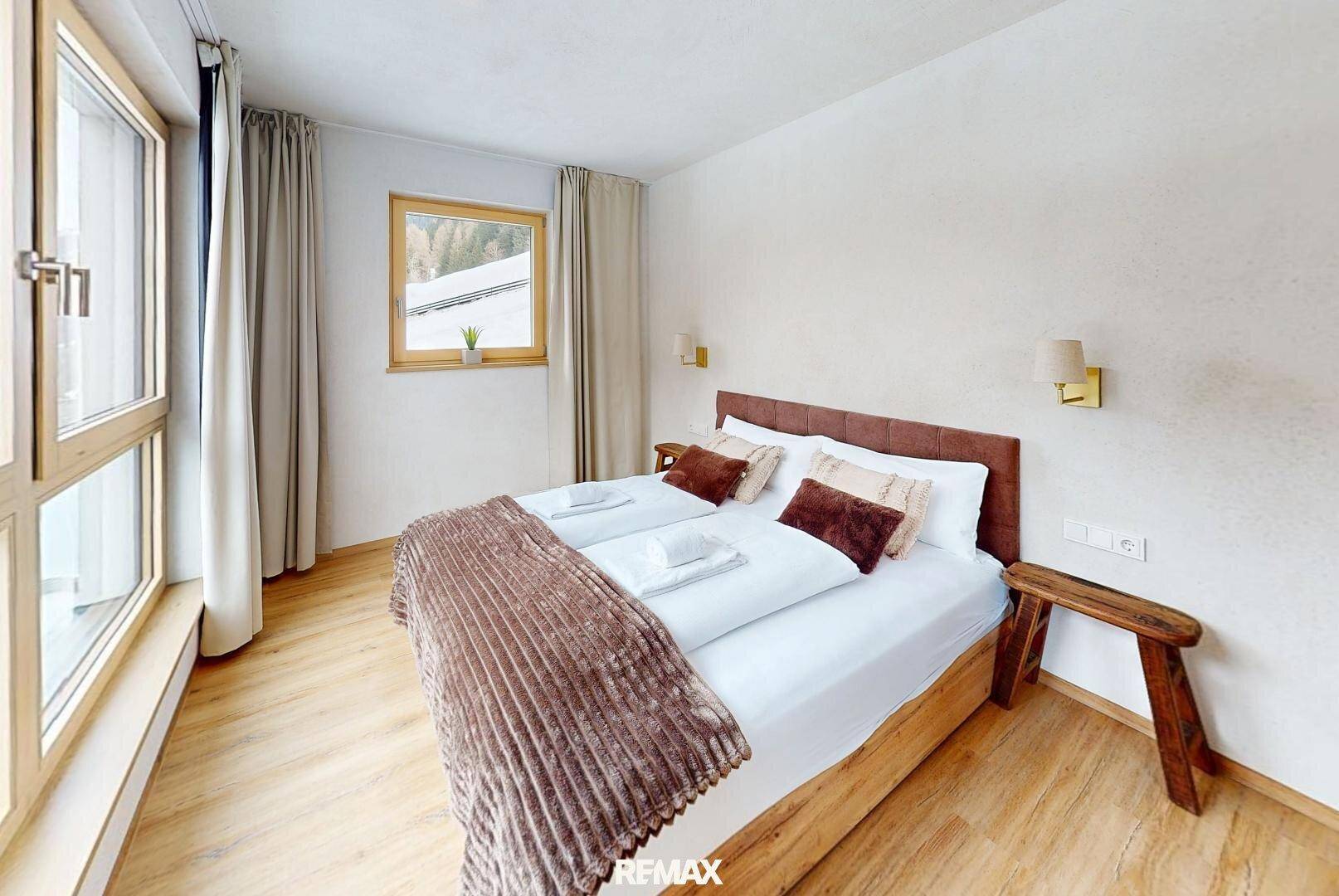 Helles Schlafzimmer mit Doppelbett, Holzboden und Fenster mit Blick nach draußen.