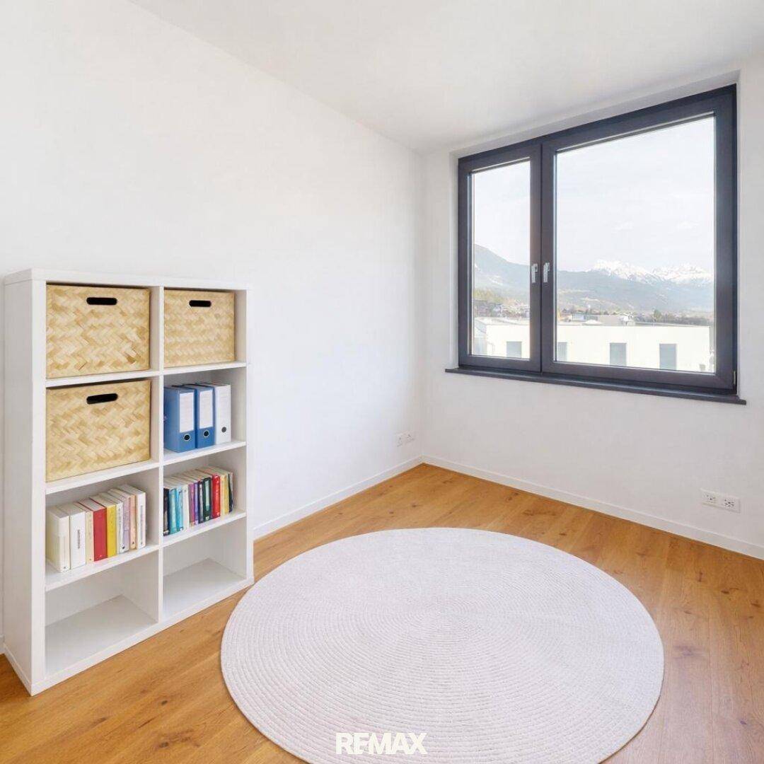 Helles Zimmer mit Holzboden, Bücherregal und einem Fenster, das einen schönen Bergblick freigibt.