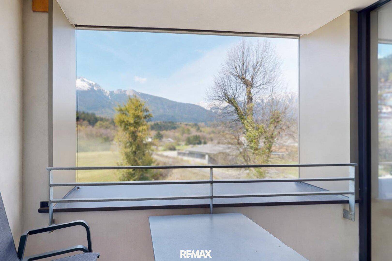 Gemütlicher Balkon mit Tisch und Stuhl, der einen weiten Blick auf die umliegende Berglandschaft bietet.
