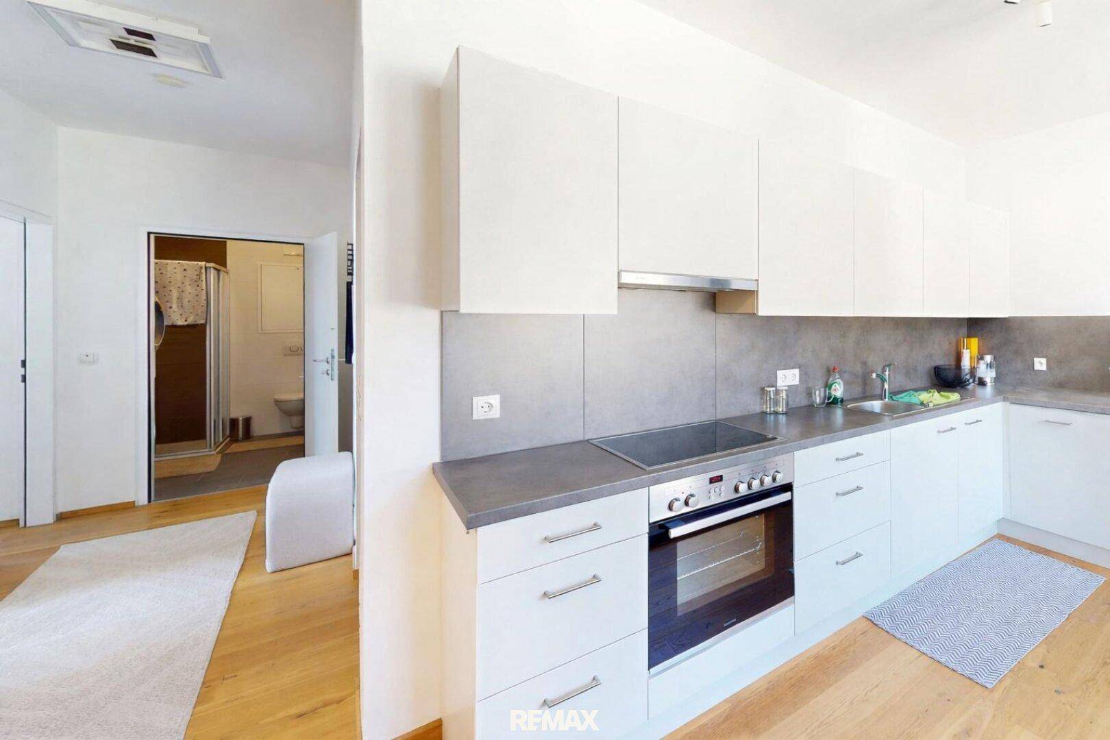 Moderne Küche mit weißen Schränken, integrierten Geräten und Blick in ein angrenzendes Badezimmer.