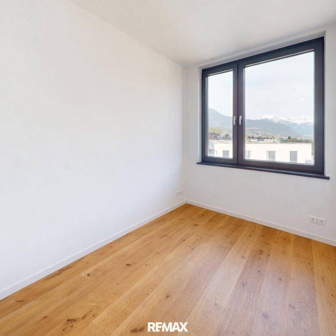 Leeres Zimmer mit hellem Holzboden und einem großen Fenster, das einen malerischen Bergblick bietet.