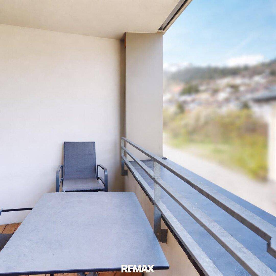 Balkon mit Sitzgelegenheiten und einer weiten Aussicht auf die grüne Umgebung und die Berge.