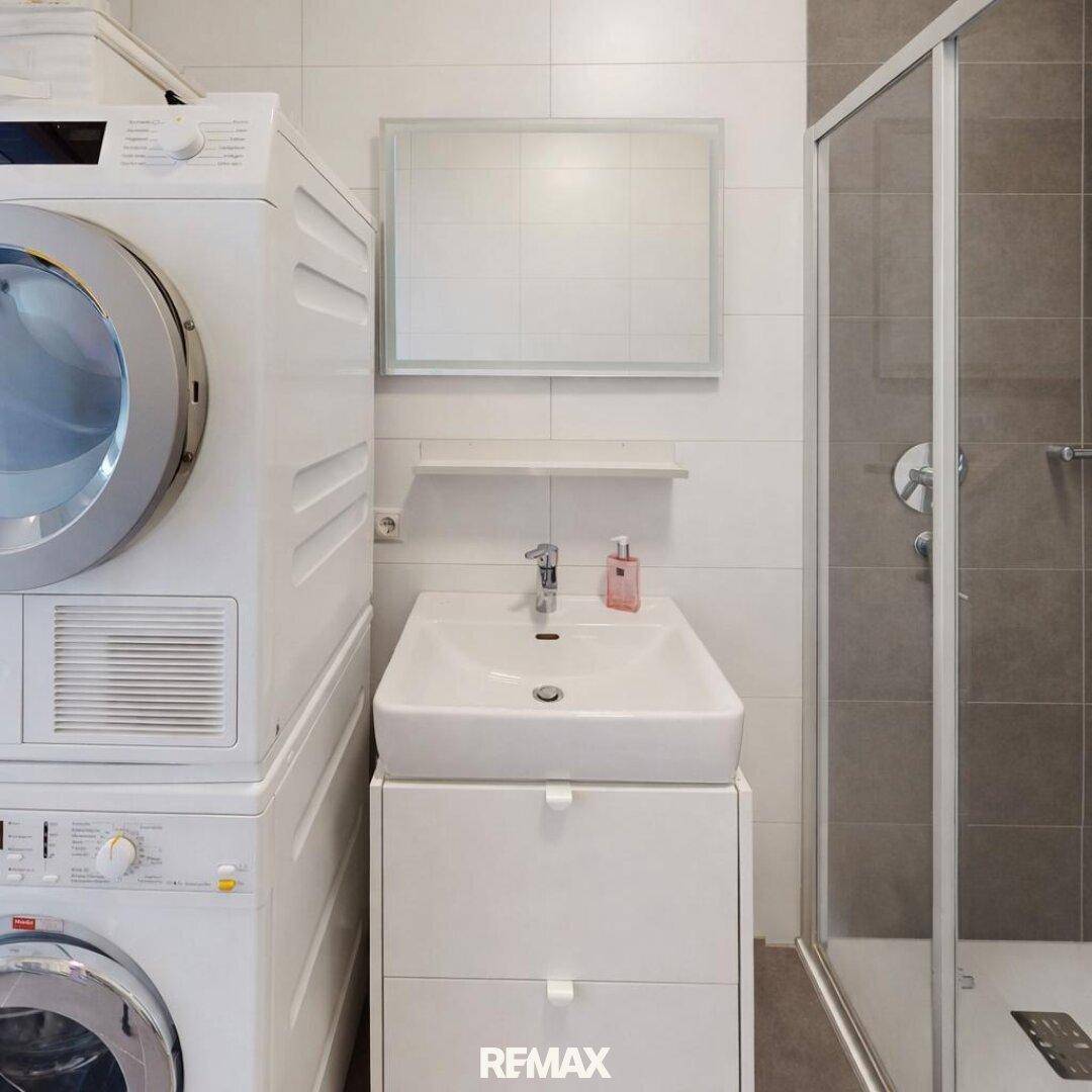 Funktionales Badezimmer mit Waschbecken, Duschkabine und praktischer Waschmaschine-Trockner-Kombination.