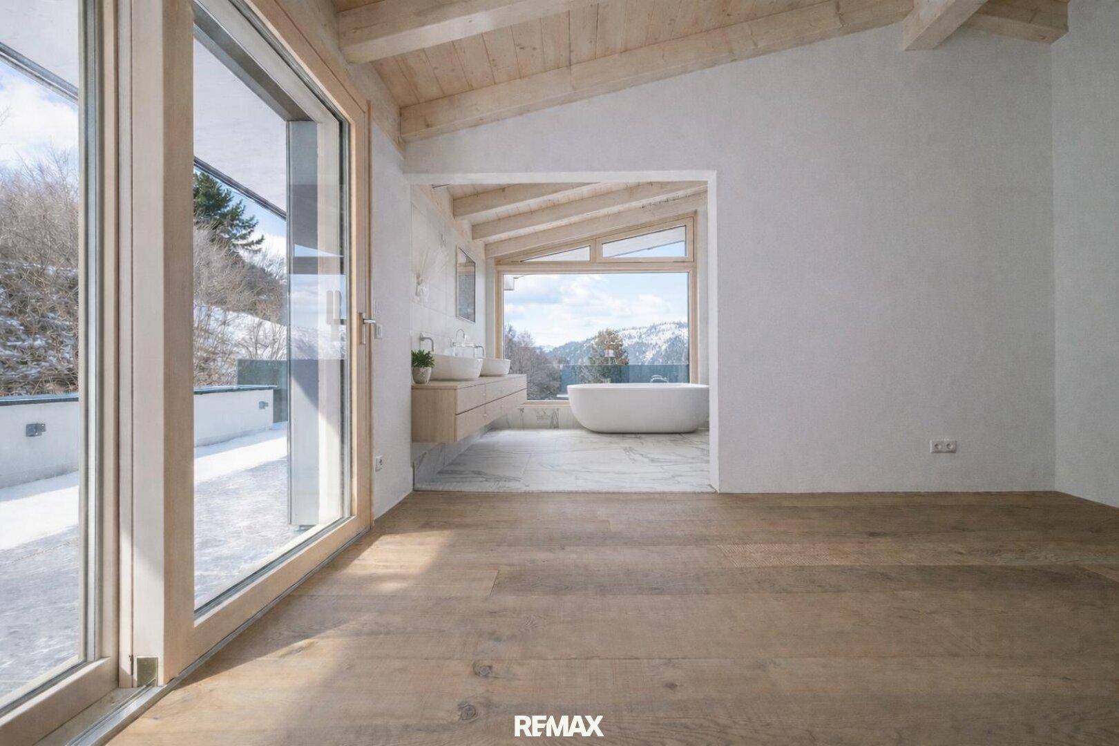 Heller Raum mit Holzboden und Holzbalkendecke, Zugang zur Terrasse und Blick auf ein Badezimmer mit Badewanne.