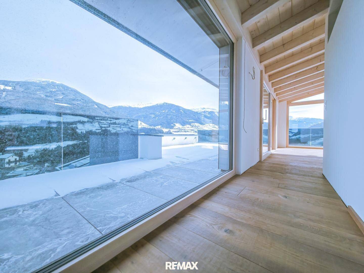 Heller Flur mit Holzboden und großen Fenstern, die einen weiten Blick auf die verschneite Landschaft bieten.