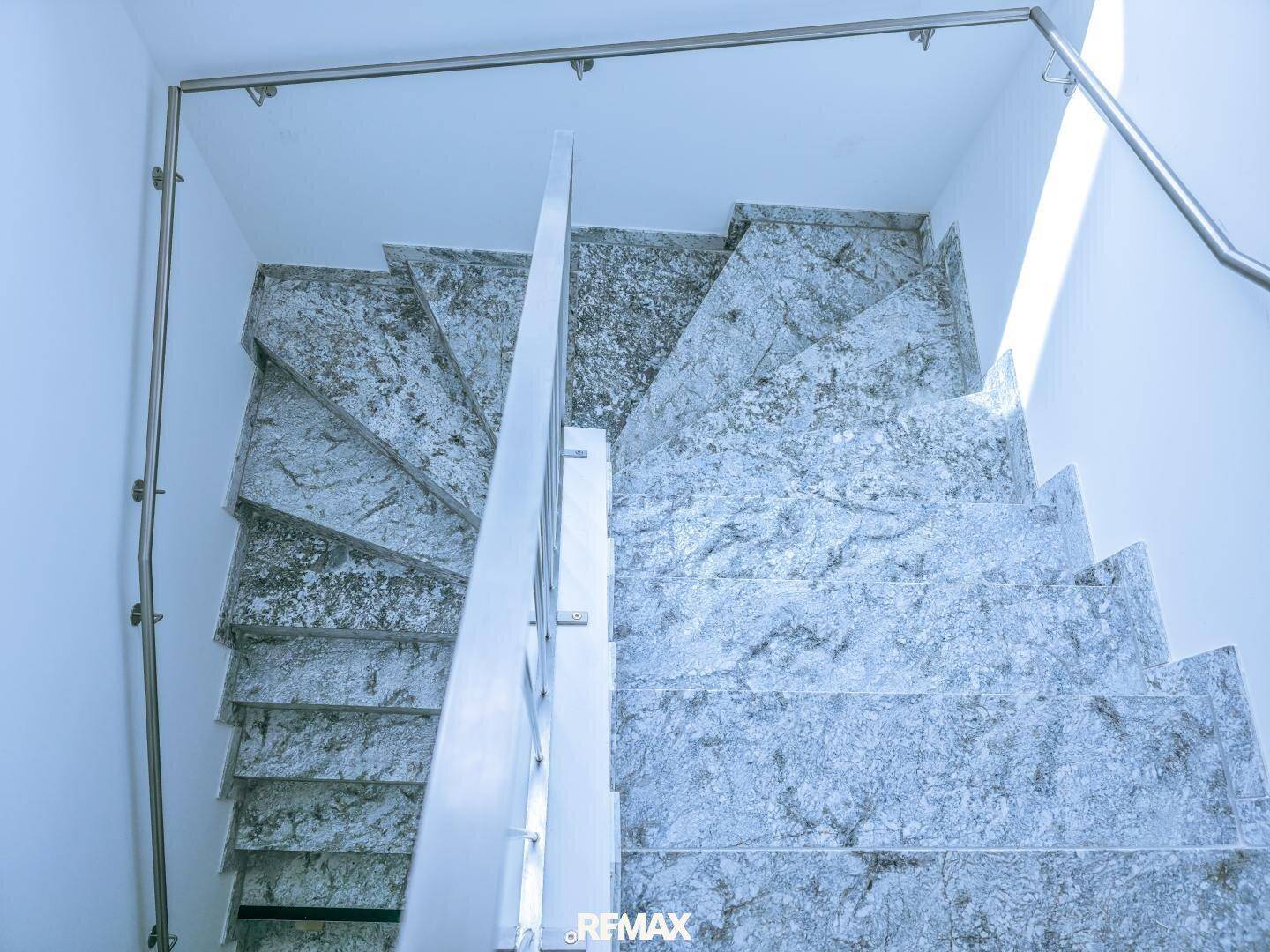 Elegante Treppe mit Granitstufen und modernem Metallgeländer, verbindet die verschiedenen Ebenen.