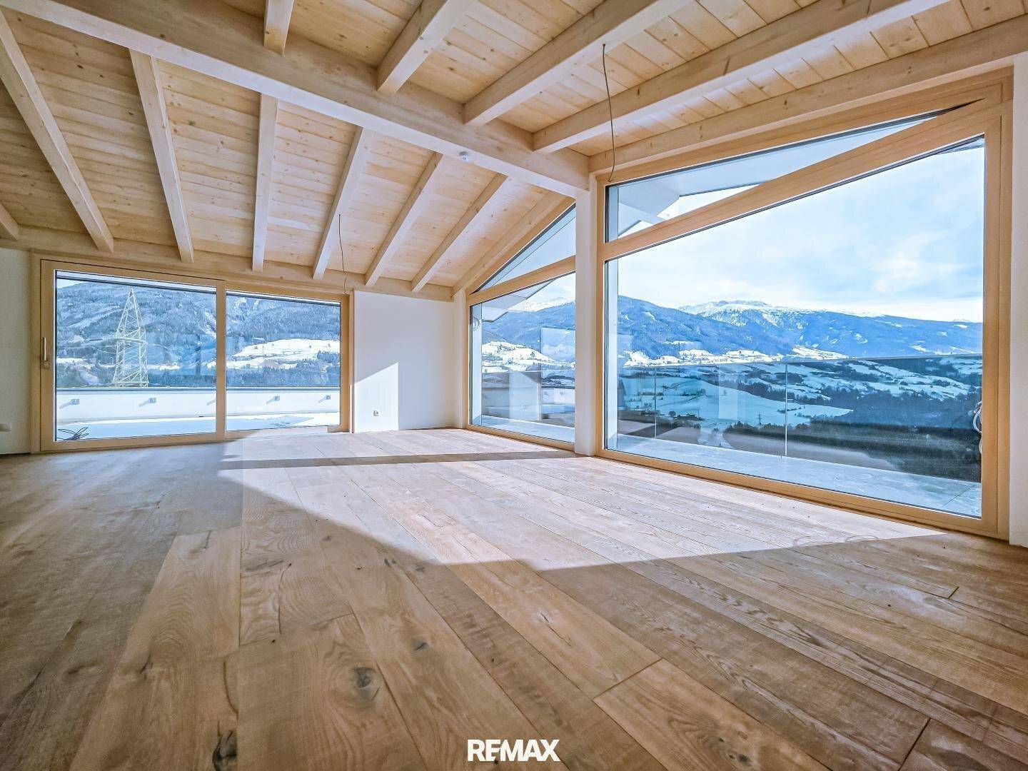 Heller Wohnraum mit Holzboden und Holzbalkendecke, großen Fenstern und beeindruckendem Bergblick.