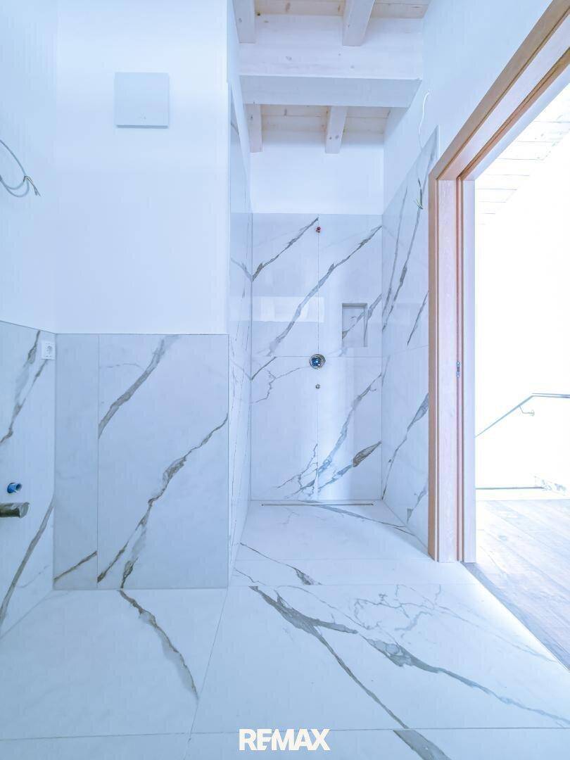 Modernes, unfertiges Badezimmer mit Marmoroptik-Fliesen und einer geräumigen begehbaren Dusche.