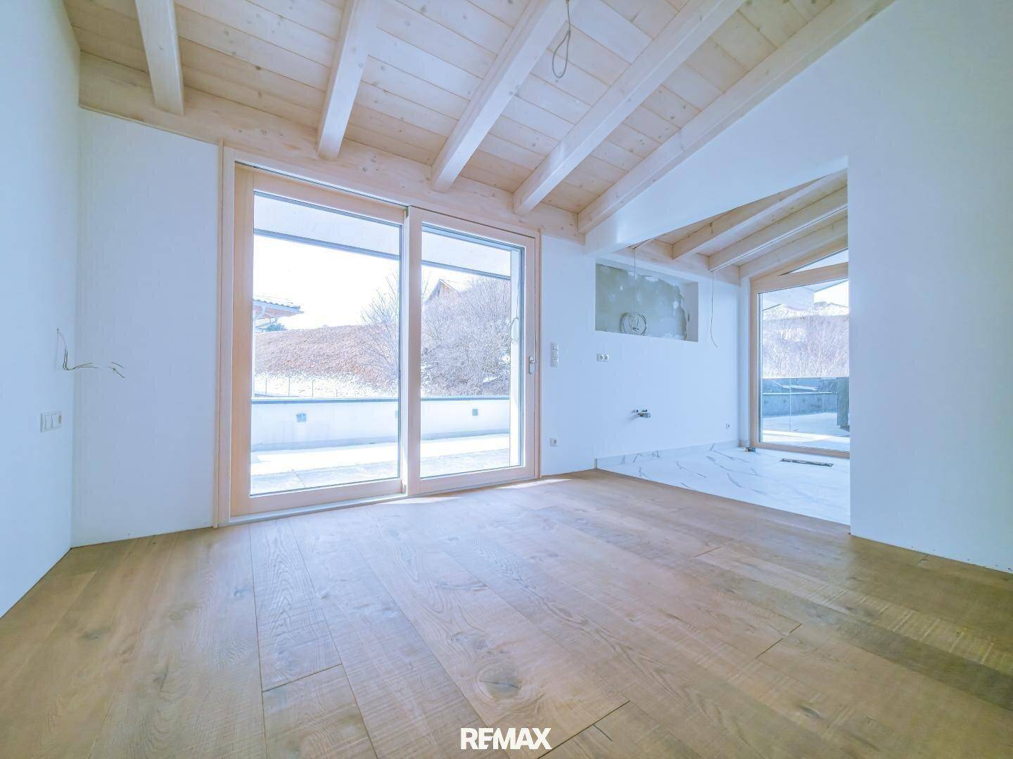 Heller Raum mit Holzboden und Holzbalkendecke, großer Schiebetür und Zugang zu einer Außenterrasse.