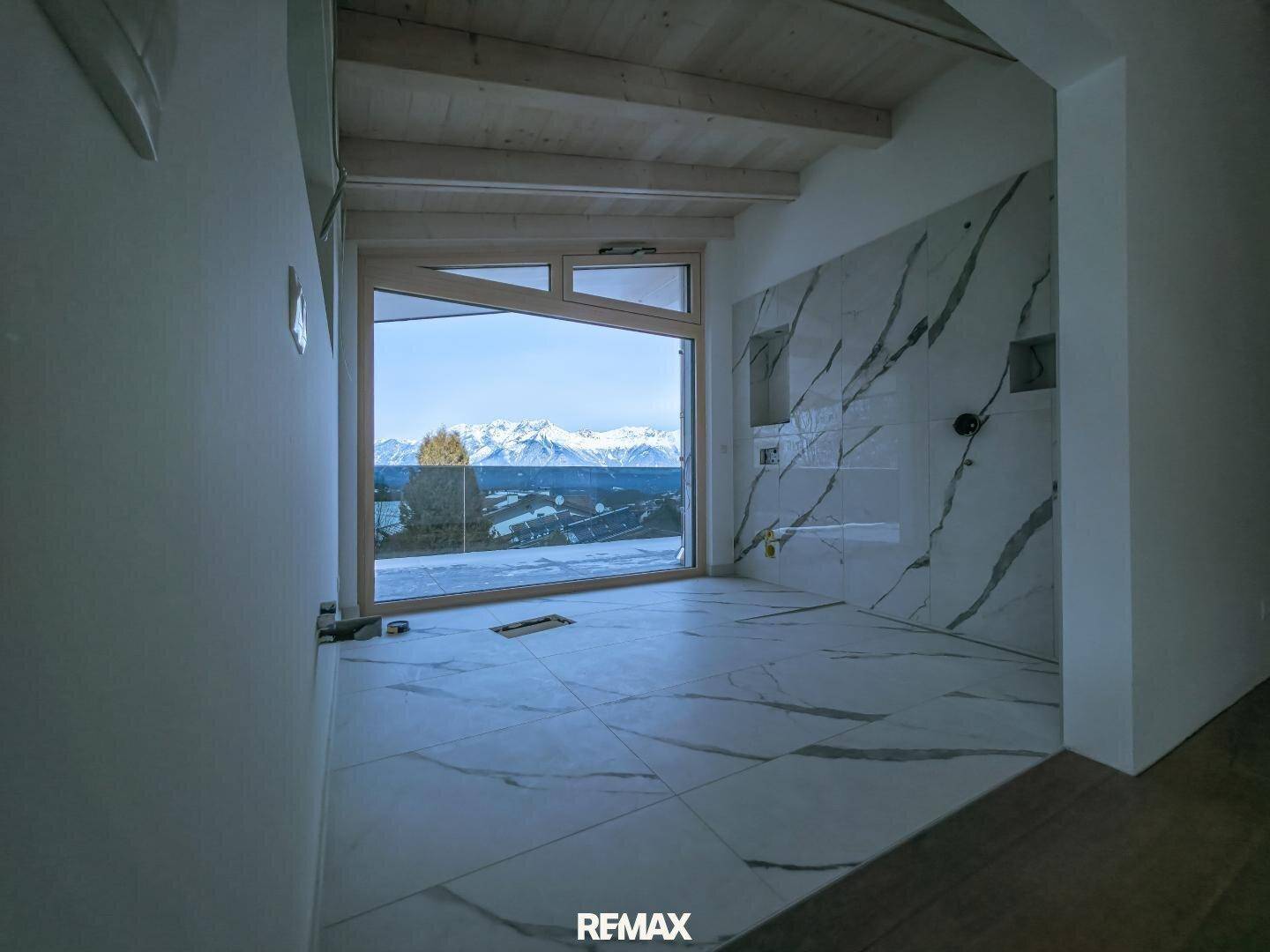 Unfertiges Badezimmer mit Marmoroptik-Fliesen, großem Fenster und beeindruckendem Bergblick.