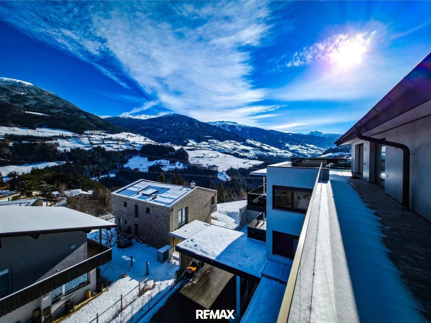 Panoramablick über eine verschneite Wohnsiedlung in den Bergen unter strahlend blauem Himmel.