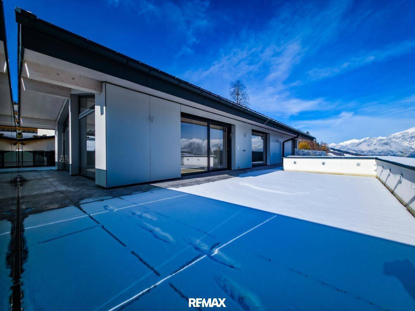 Weitläufige, schneebedeckte Terrasse mit großen Fenstern und Blick auf die umliegende Berglandschaft.