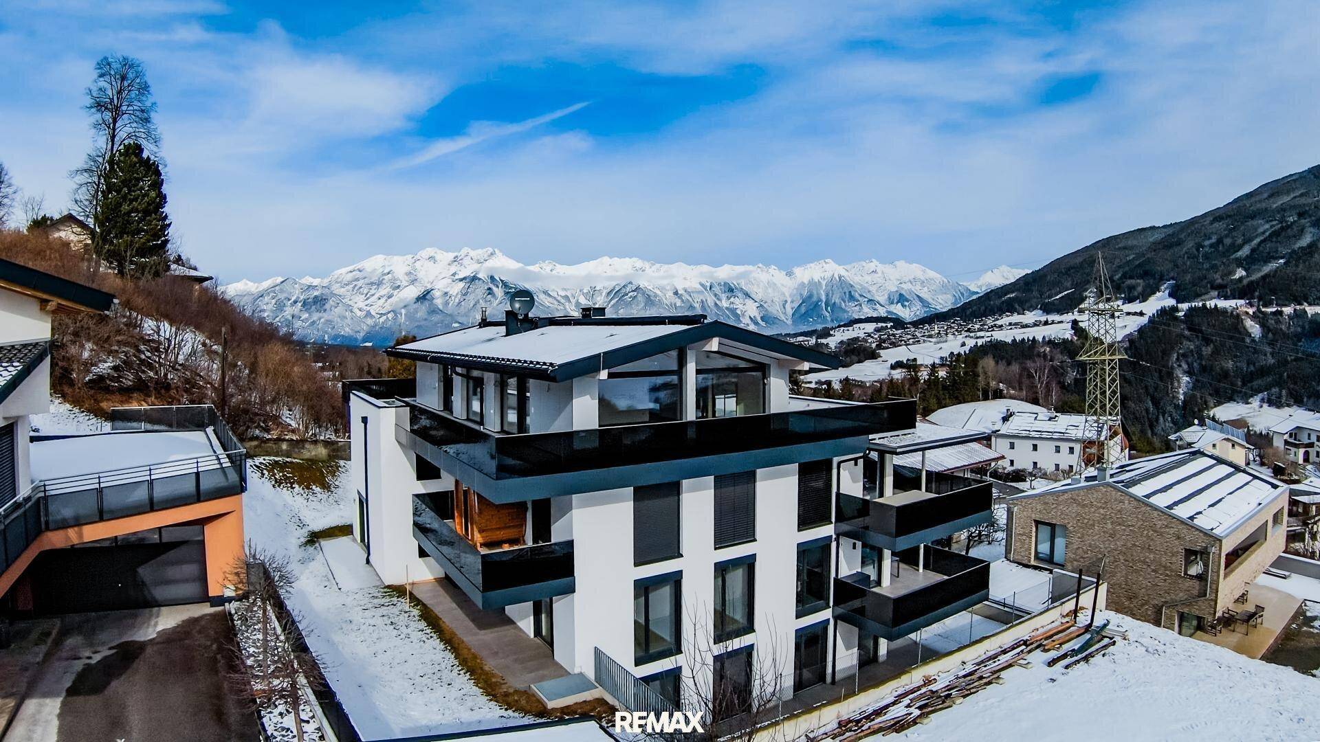 Moderne Architektur eines Mehrfamilienhauses in einer verschneiten Berglandschaft mit weitem Blick.