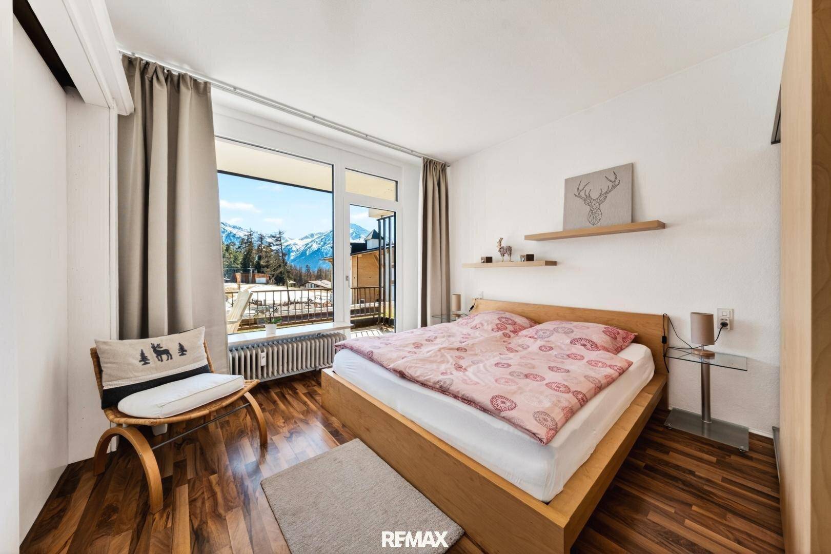 Gemütliches Schlafzimmer mit Holzbett, Parkettboden und Zugang zum Balkon mit Bergsicht.
