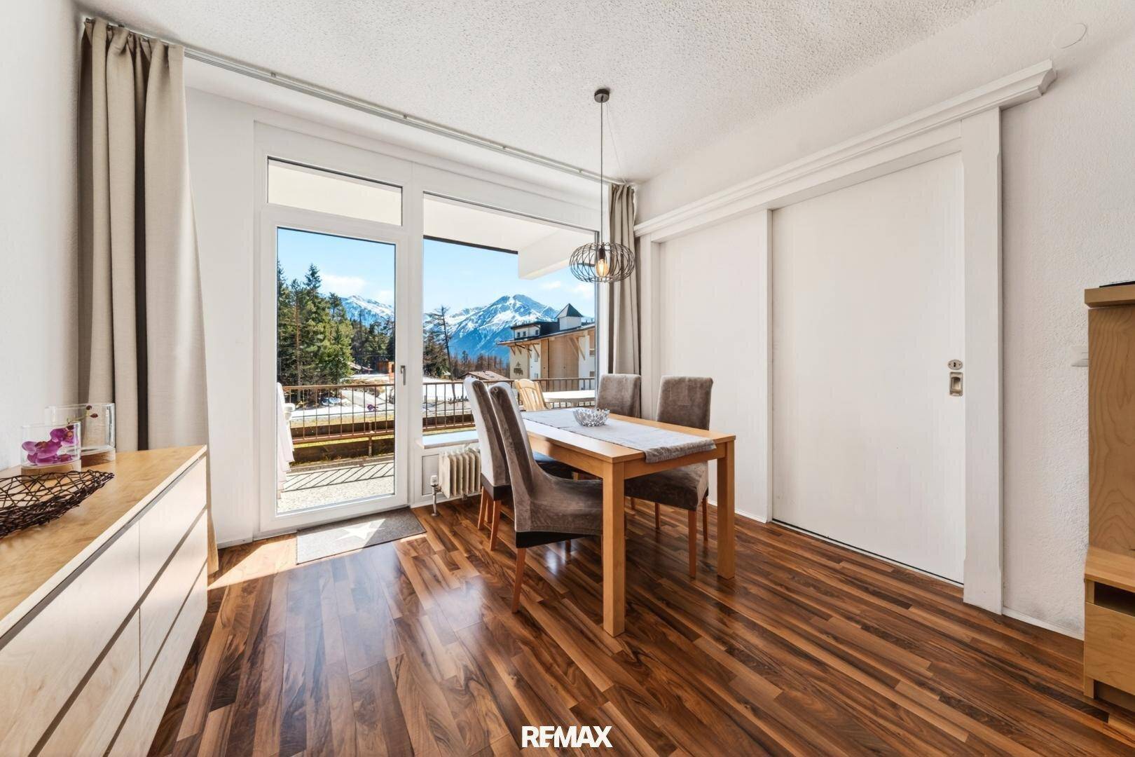 Einladender Essbereich mit Holzboden und großem Fenster, das einen malerischen Blick auf die Berge bietet.