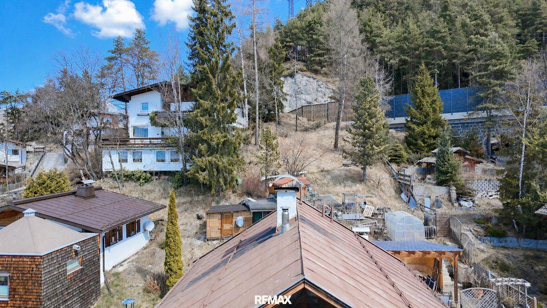 Häuser am steilen Hang, umgeben von Wald und mit Blick auf die umliegende Bergwelt.