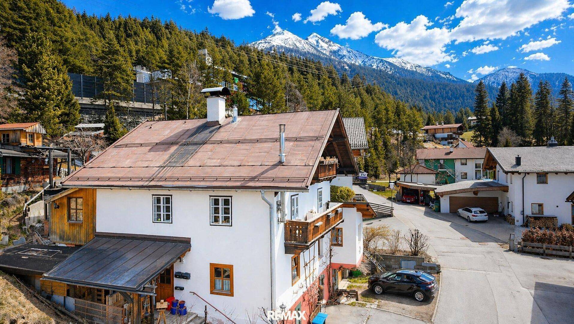 Traditionelles Wohnhaus mit kleinem Balkon, gepflasterter Straße und beeindruckendem Bergblick.