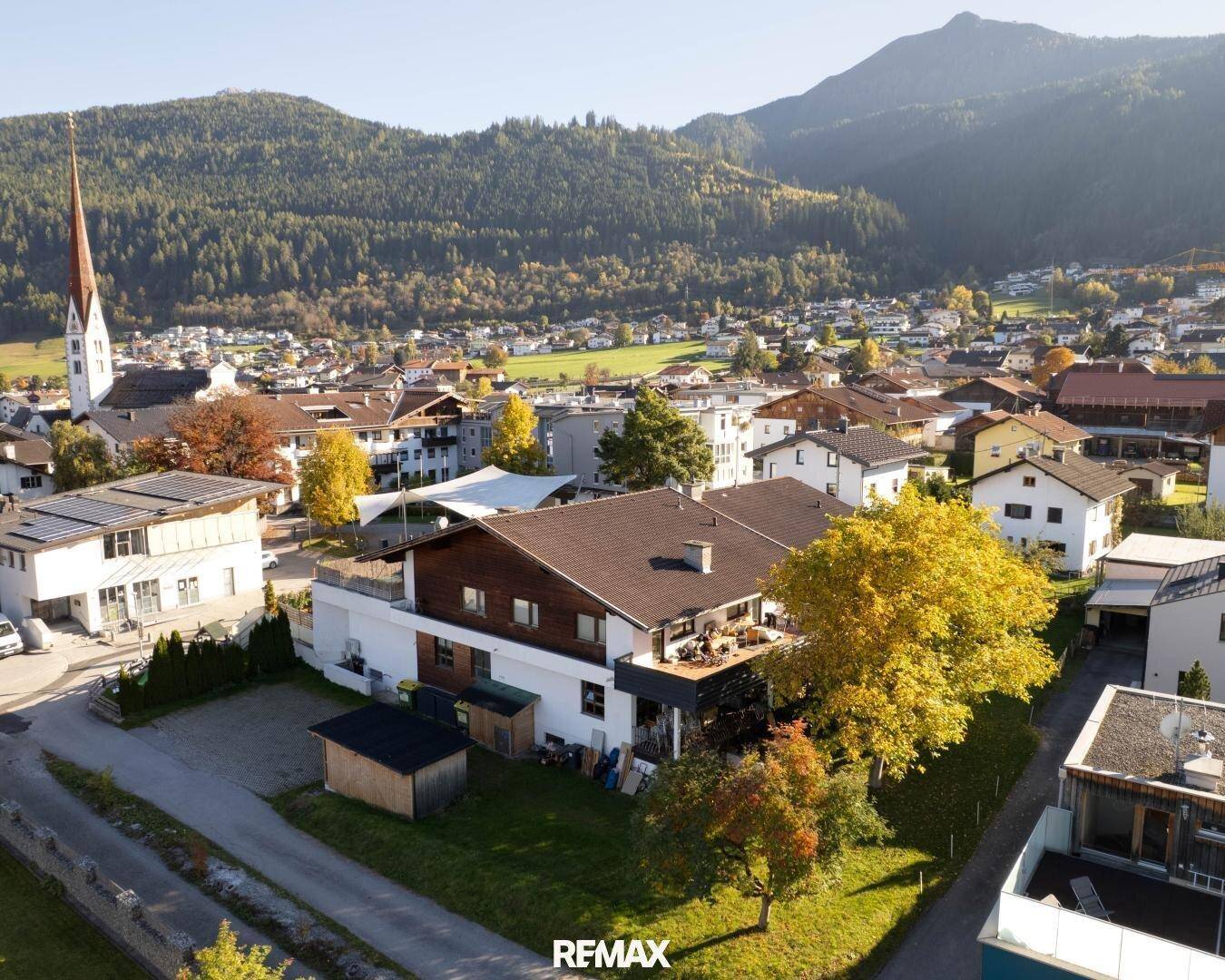 Panoramablick auf eine ländliche Wohnsiedlung mit Kirche, umgeben von Bergen und einem Haus mit Balkon.
