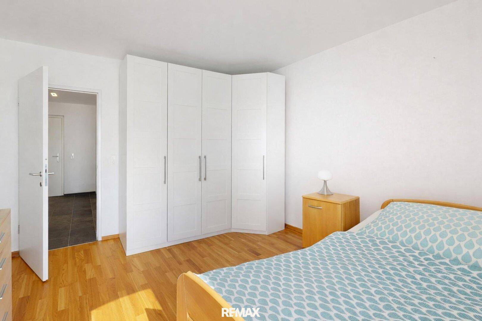 Schlafzimmer mit hellem Parkettboden und einem großen weißen Eckkleiderschrank.