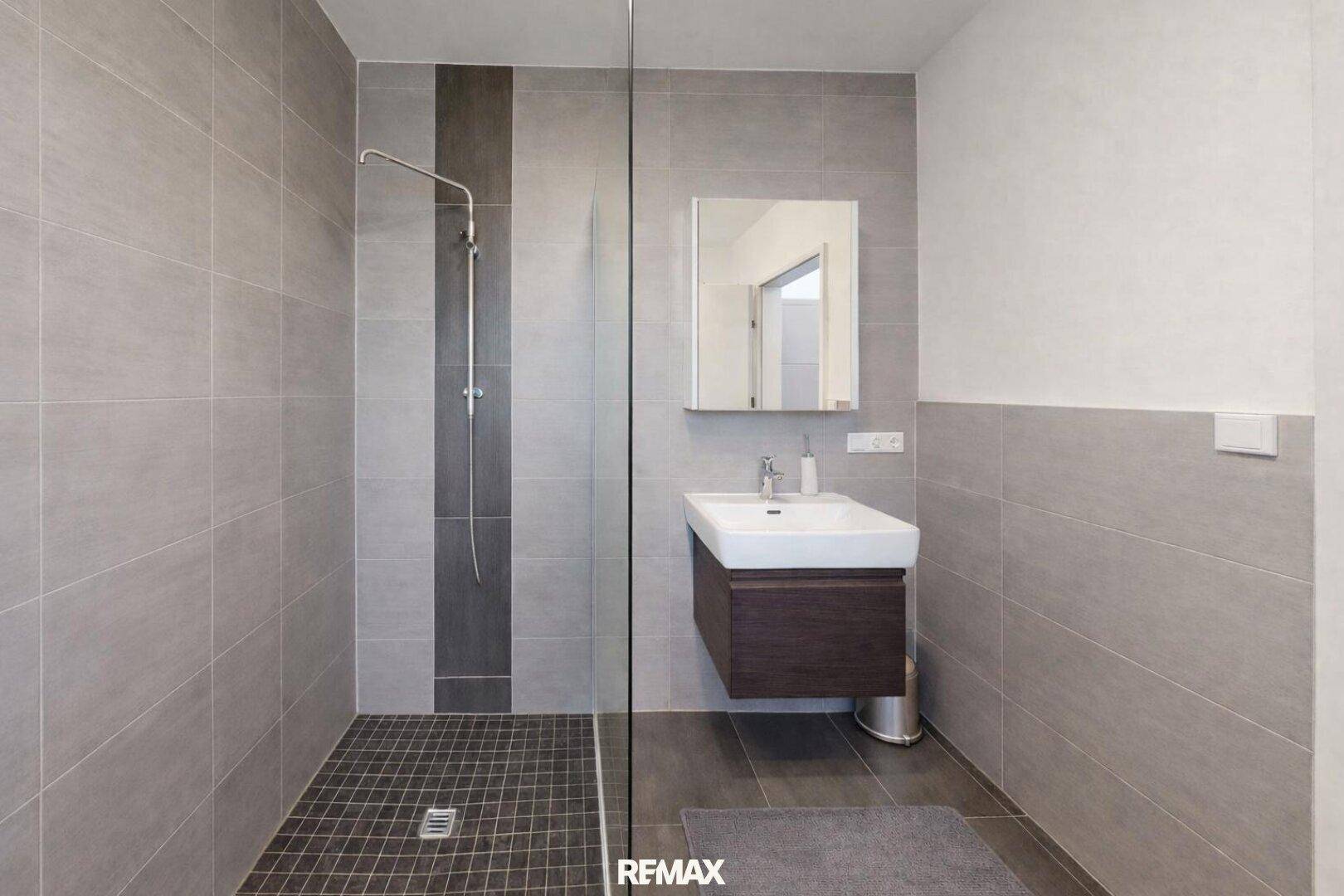 Modernes Badezimmer mit ebenerdiger Dusche, grauen Fliesen und schwebendem Waschtisch.