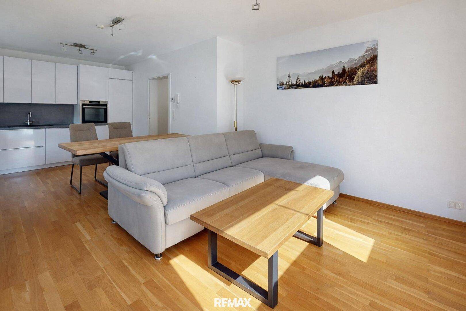 Helles Wohn- und Esszimmer mit offener Küche, Parkettboden und modernem Sofa.