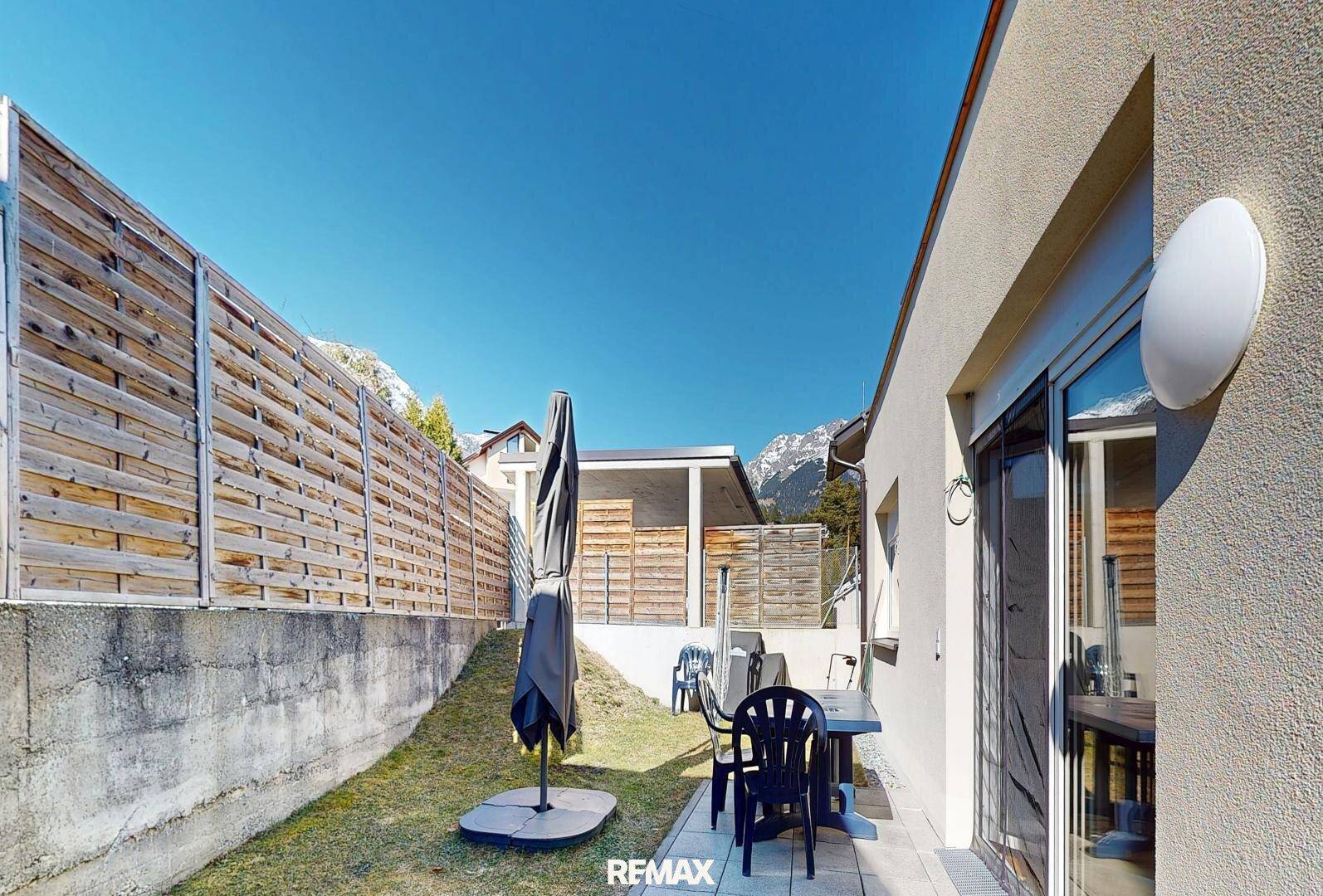 Sonniger Gartenbereich mit Terrasse, Sitzgelegenheiten und Blick auf die Berge.