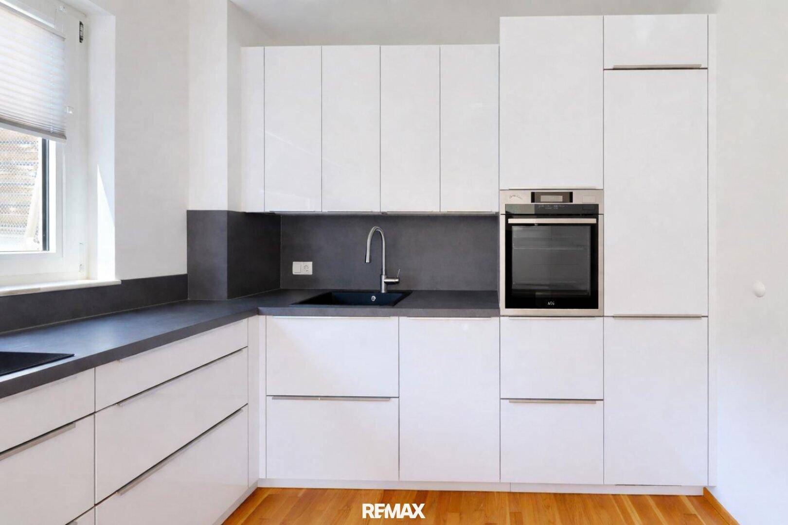 Moderne Einbauküche mit weißen Hochglanzfronten, dunkler Arbeitsplatte und integriertem Backofen.