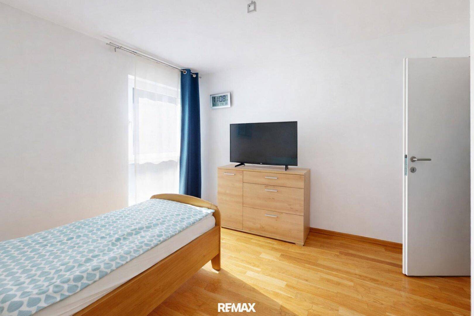 Helles Schlafzimmer mit Holzbett, Parkettboden und einem Fernseher auf einer Kommode.