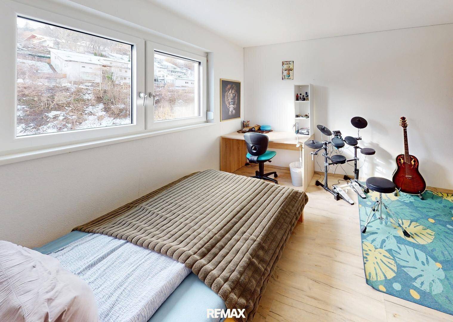 Helles Schlafzimmer mit Einzelbett, Schreibtisch, Musikinstrumenten und Blick ins Grüne.