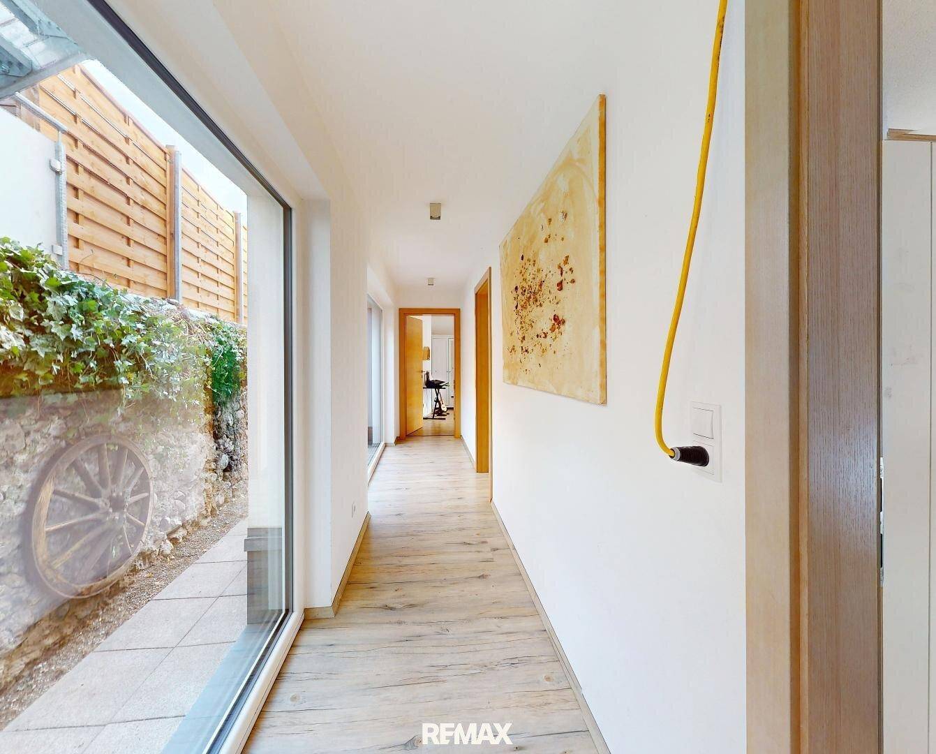 Langer, heller Flur mit Laminatboden und großen Fenstern, die viel Tageslicht hereinlassen.