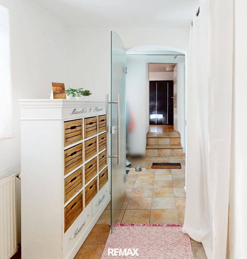 Heller Flur mit Fliesenboden, einem dekorativen Schrank und einer modernen Glastür.