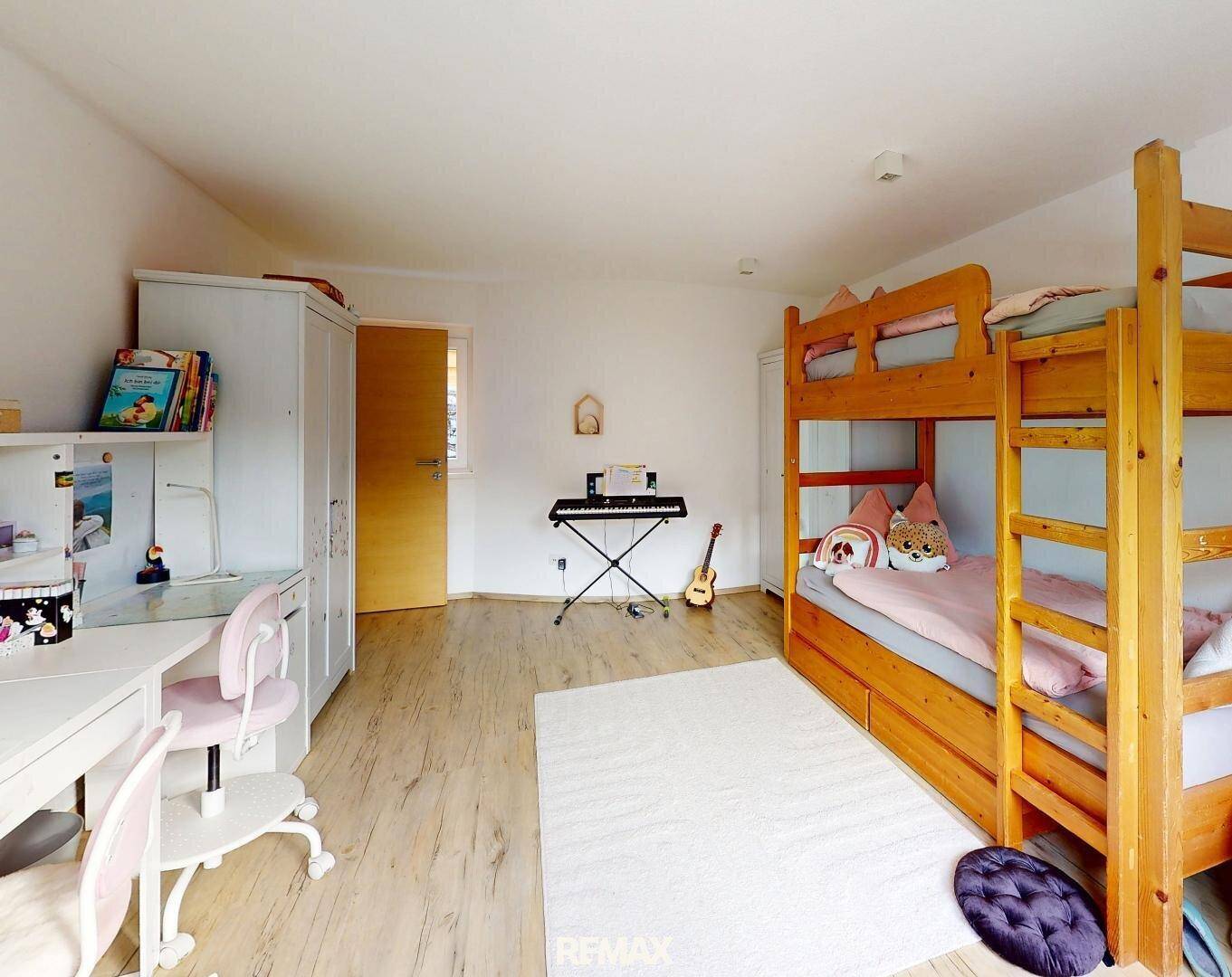 Kinderzimmer mit Etagenbett, Schreibtisch, Kleiderschrank und Musikinstrumenten auf hellem Laminatboden.