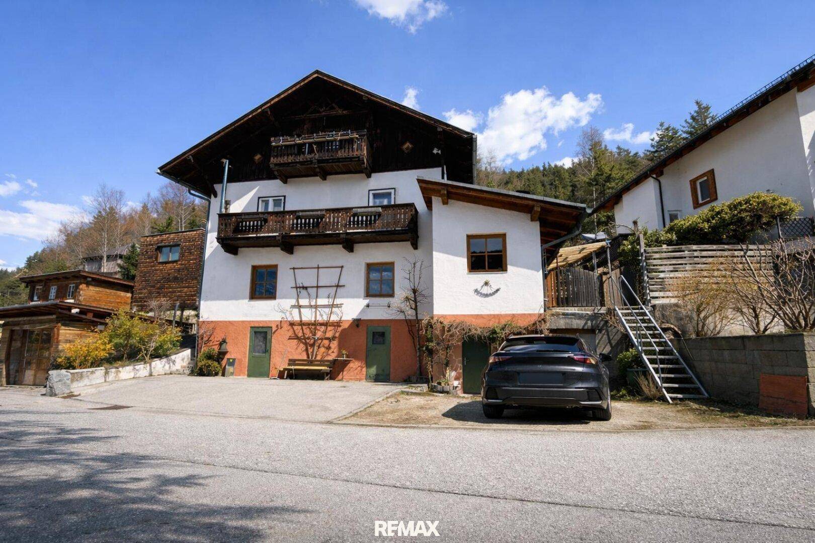 Traditionelles Haus im alpinen Stil mit Holzbalkonen und einer Zufahrt im ländlichen Umfeld.