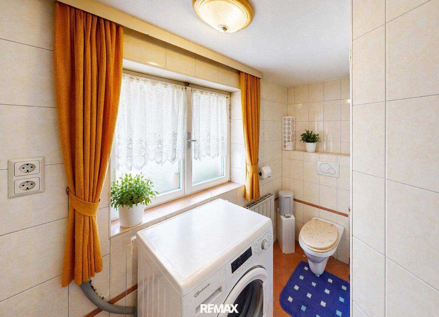 Kleiner Waschraum oder Badezimmer mit Toilette, Waschmaschine und einem Fenster, komplett gefliest.
