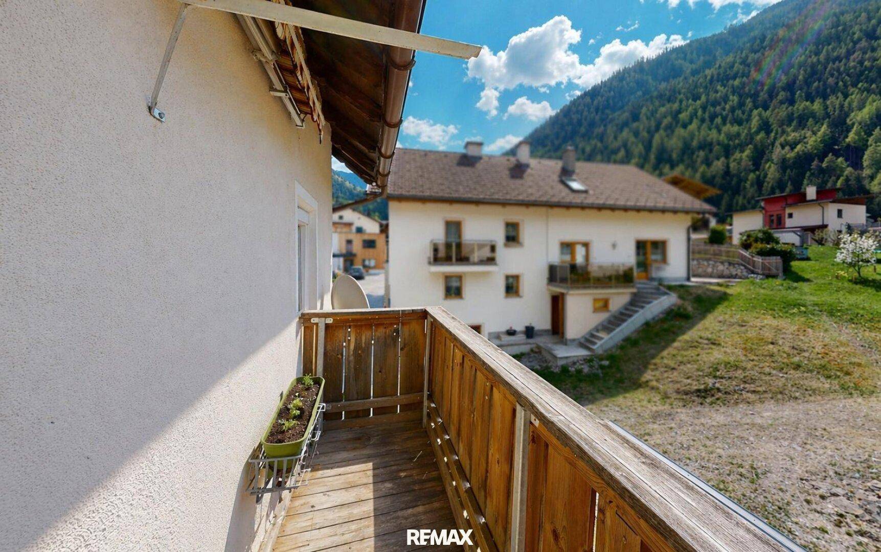 Kleiner Holzbalkon mit Ausblick auf weitere Häuser und die beeindruckende Berglandschaft.